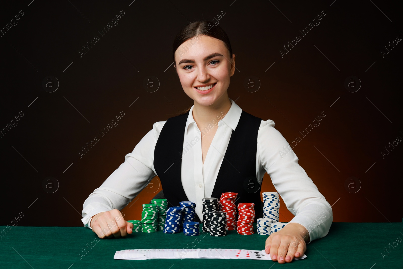 Photo of Professional croupier with casino chips and playing cards at gambling table on color background