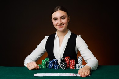 Photo of Professional croupier with casino chips and playing cards at gambling table on color background