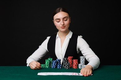 Professional croupier with casino chips and playing cards at gambling table on black background