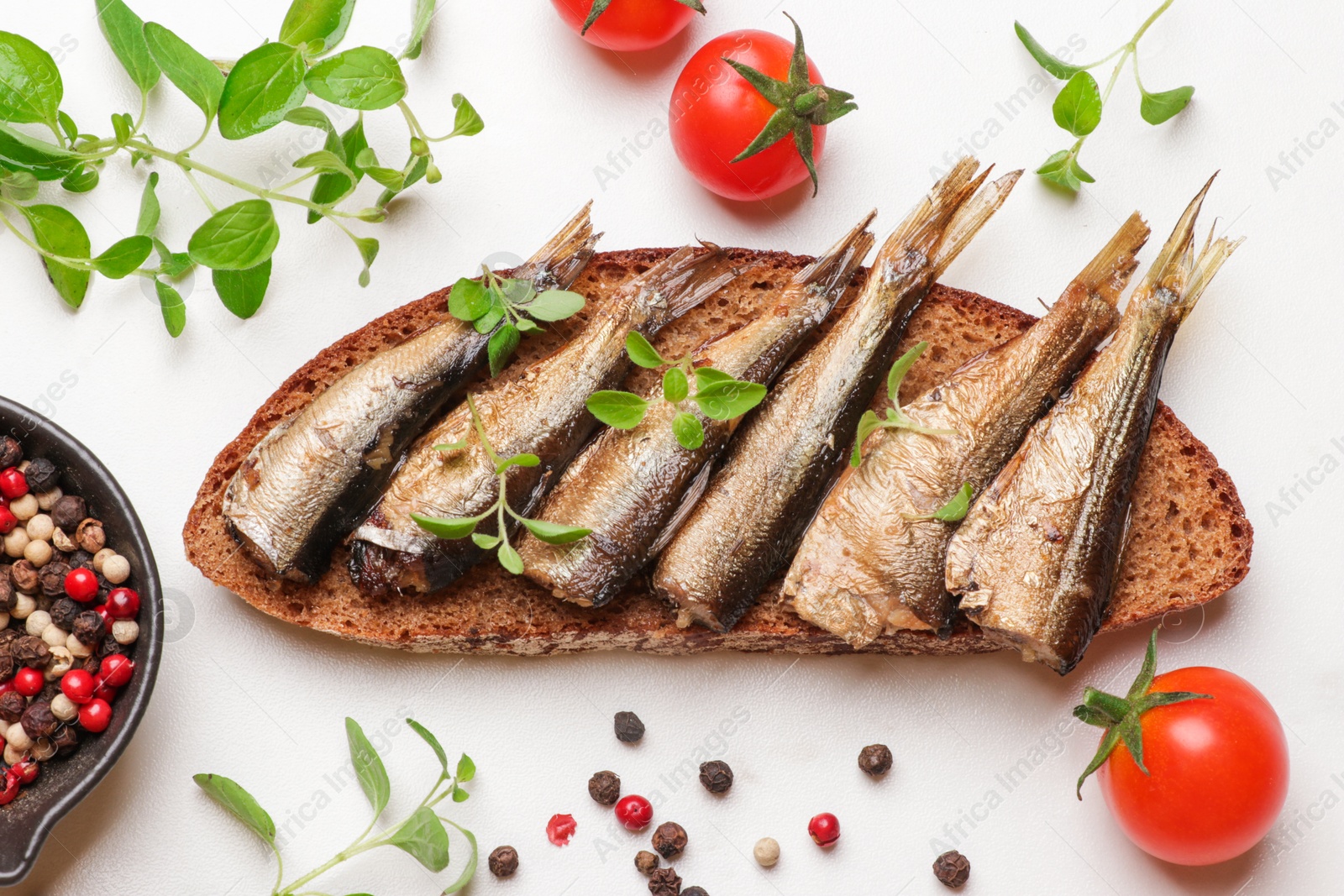 Photo of Delicious sandwich with sprats, microgreens, tomatoes and peppercorns on white table, top view