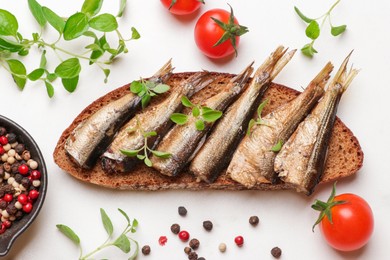 Photo of Delicious sandwich with sprats, microgreens, tomatoes and peppercorns on white table, top view