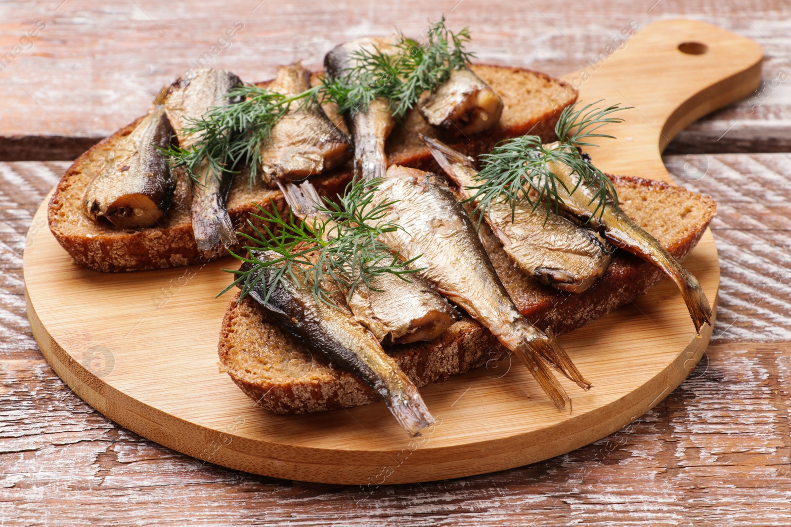 Photo of Delicious sandwiches with sprats and dill on wooden table, closeup