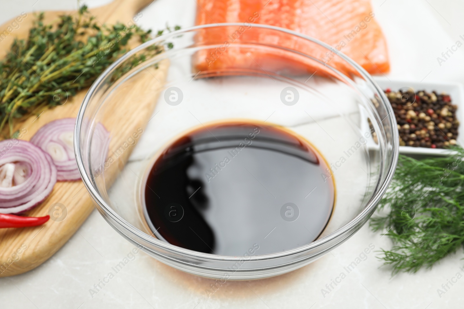 Photo of Soy sauce in bowl, salmon fillet and spices on gray marble table, closeup