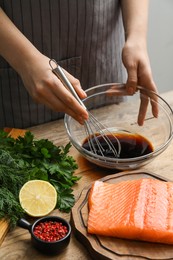 Photo of Woman making soy marinade for salmon fillet at wooden table, closeup