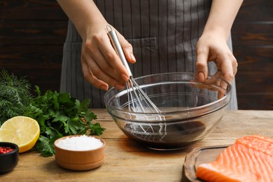 Photo of Woman making soy marinade for salmon fillet at wooden table, closeup