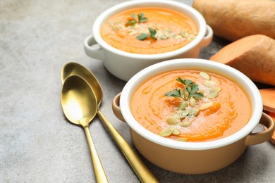 Photo of Delicious sweet potato soup with pumpkin seeds in bowls and fresh vegetables on grey textured table, closeup
