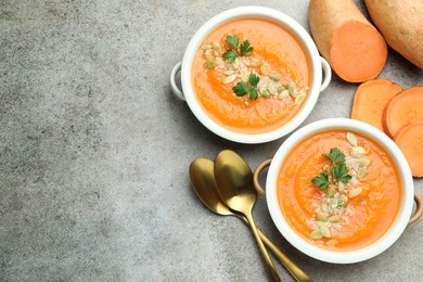 Photo of Delicious sweet potato soup with pumpkin seeds in bowls and fresh vegetables on grey textured table, flat lay. Space for text