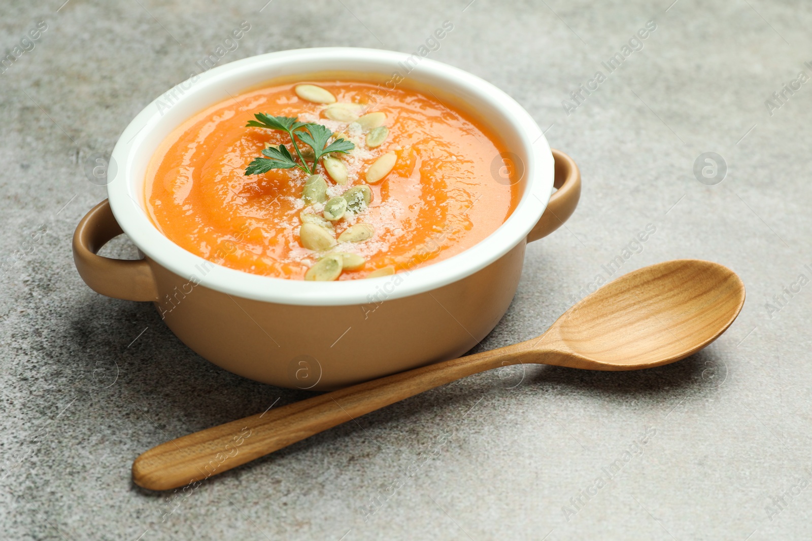 Photo of Delicious sweet potato soup with pumpkin seeds and parsley in bowl served on grey textured table, closeup
