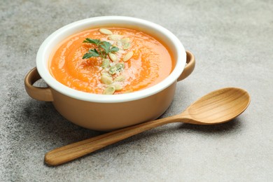 Photo of Delicious sweet potato soup with pumpkin seeds and parsley in bowl served on grey textured table, closeup