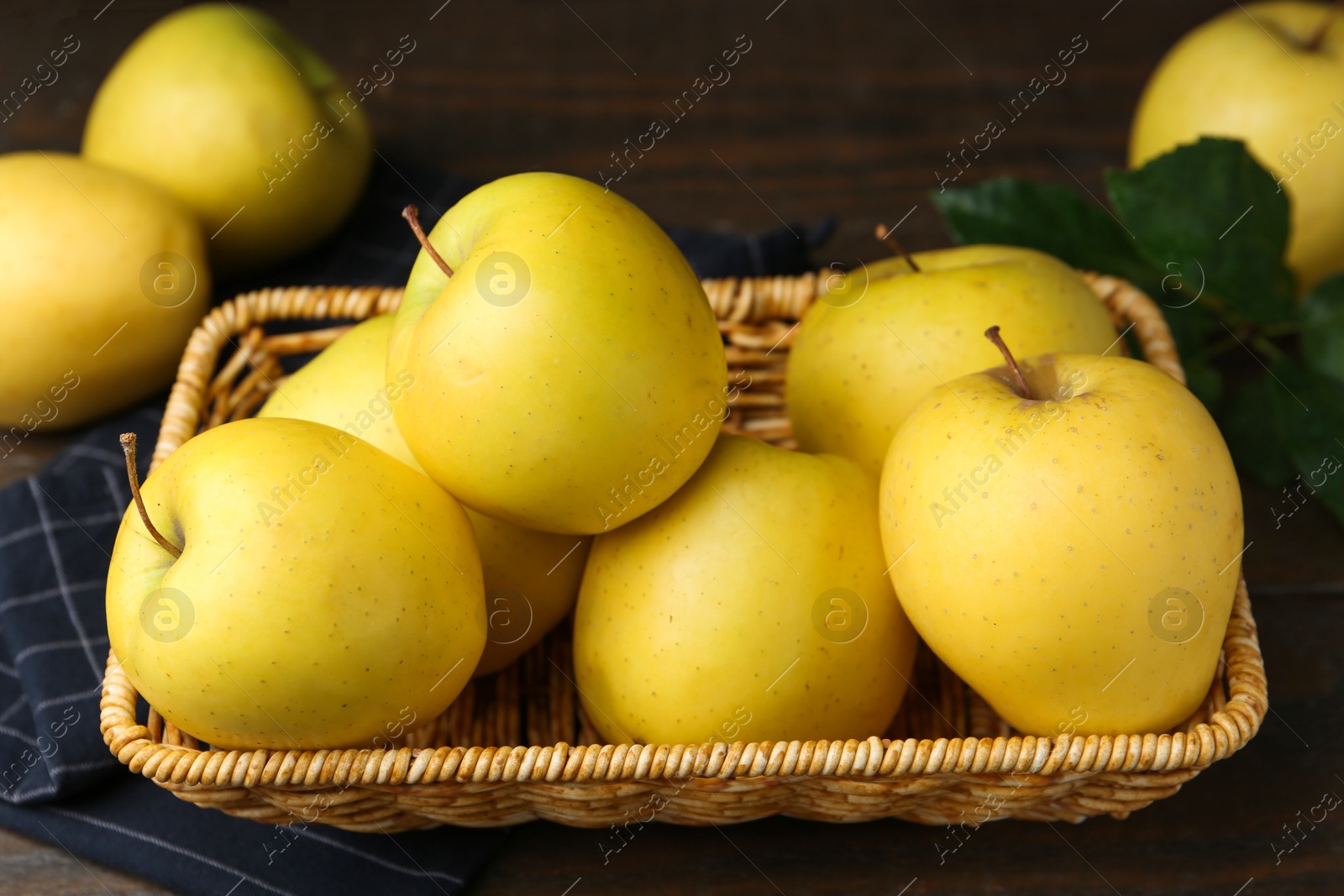 Photo of Fresh yellow apples in wicker basket on table, closeup