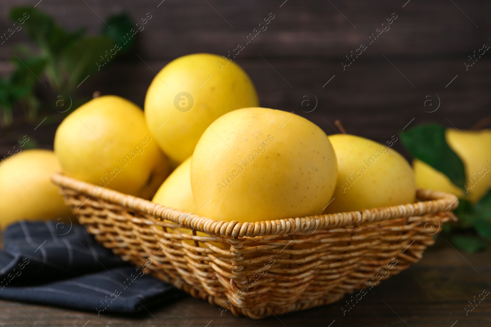 Photo of Fresh yellow apples in wicker basket on table, closeup