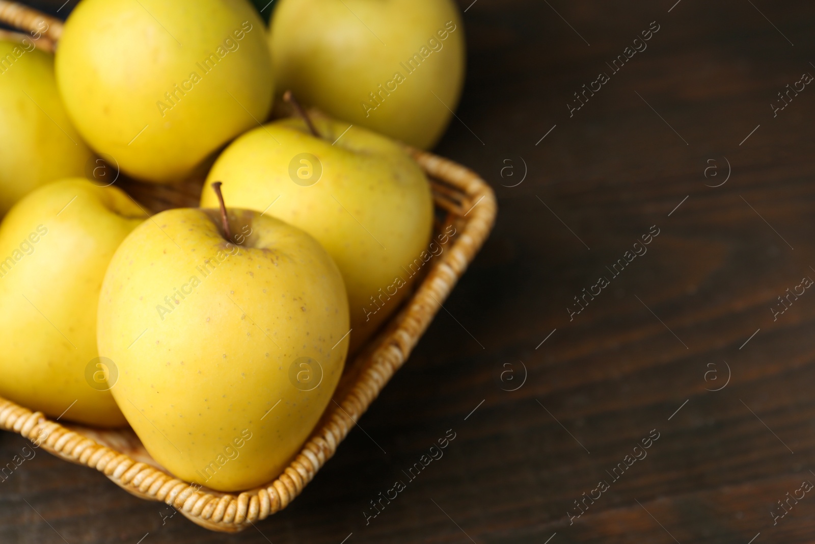 Photo of Fresh yellow apples in wicker basket on wooden table, closeup. Space for text