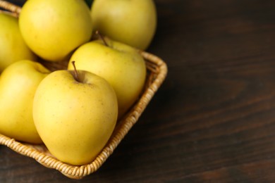 Photo of Fresh yellow apples in wicker basket on wooden table, closeup. Space for text