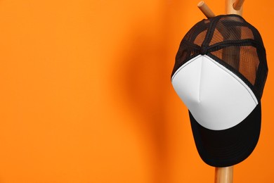 Photo of Stylish baseball cap on coat rack against orange wall. Mockup for design