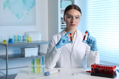 Photo of Laboratory testing. Doctor holding test tubes with blood samples at table indoors