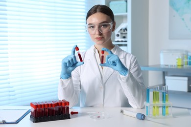 Photo of Laboratory testing. Doctor holding test tubes with blood samples at table indoors