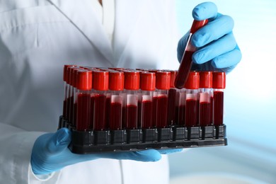 Photo of Laboratory testing. Doctor taking test tube with blood sample from rack indoors, closeup