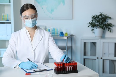 Laboratory testing. Doctor taking test tube with blood sample while working at table indoors