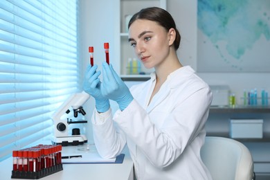 Photo of Laboratory testing. Doctor holding test tubes with blood samples at table indoors