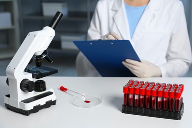 Photo of Laboratory testing. Doctor working at table indoors, focus on microscope and blood samples