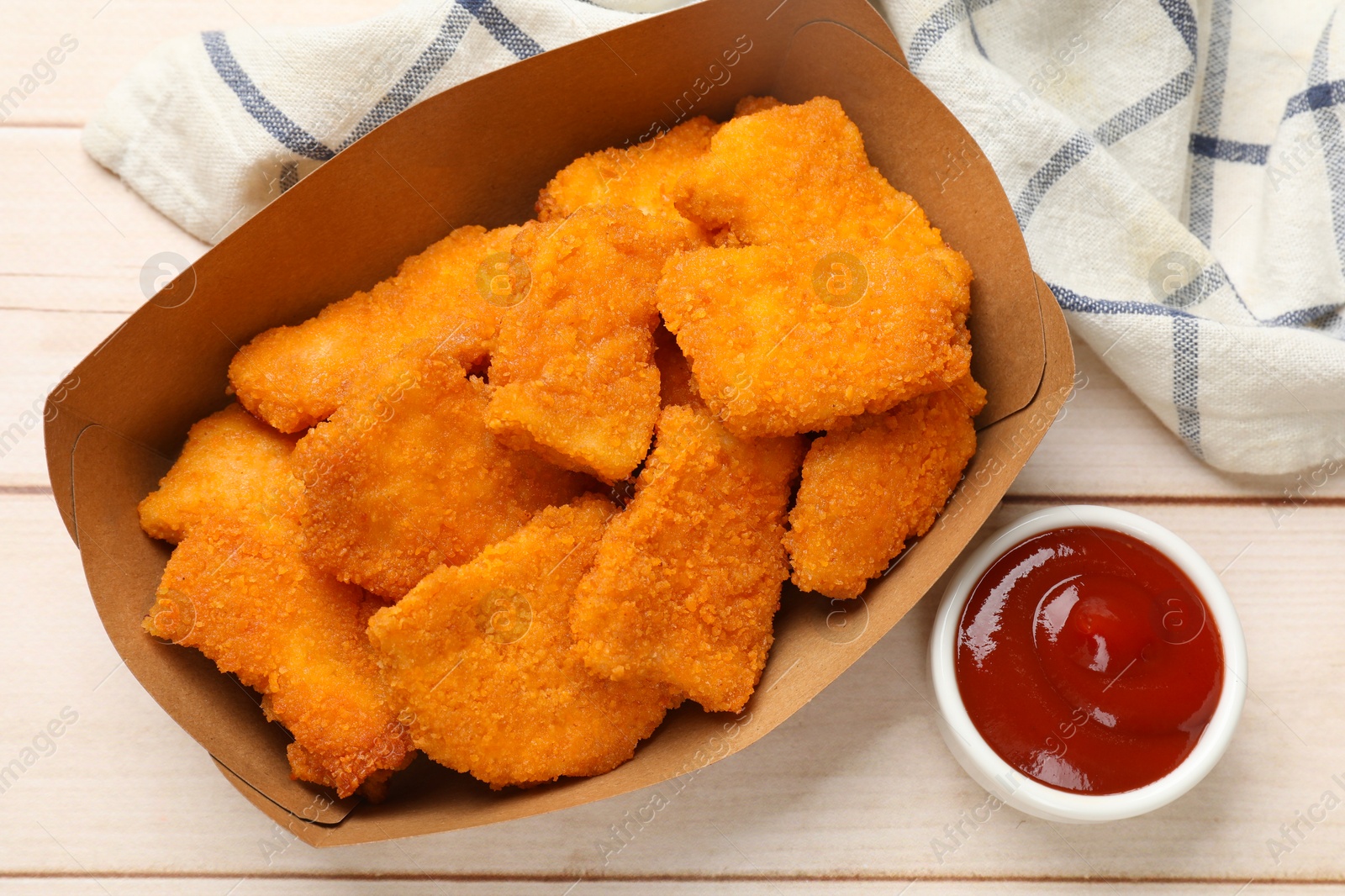 Photo of Tasty chicken nuggets in paper container and sauce on wooden table, top view