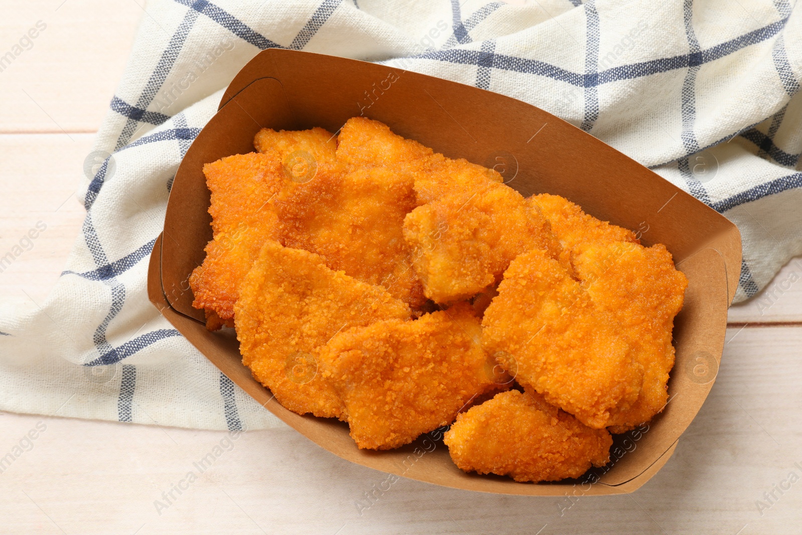 Photo of Tasty chicken nuggets in paper container on wooden table, top view