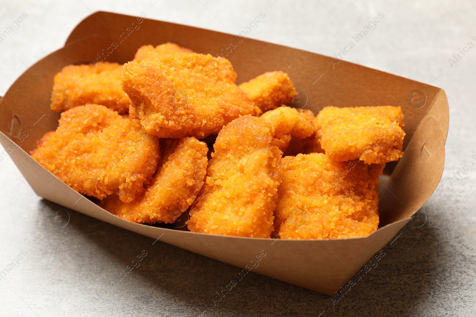 Photo of Delicious chicken nuggets in carton box on light table, closeup