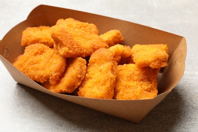 Photo of Delicious chicken nuggets in carton box on light table, closeup