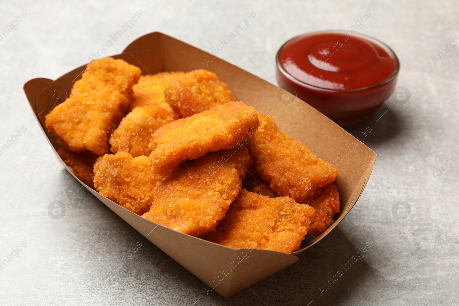 Photo of Delicious chicken nuggets in carton box and ketchup on light table, closeup