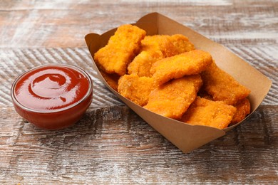 Photo of Delicious chicken nuggets with ketchup on wooden table, closeup