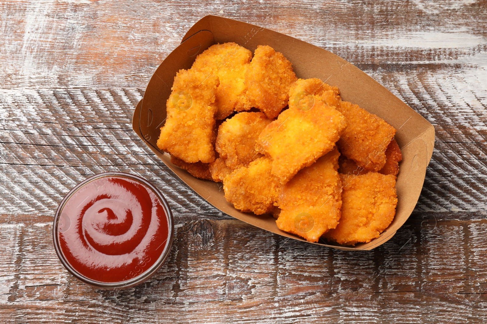 Photo of Delicious chicken nuggets with ketchup on wooden table, top view