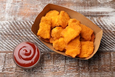 Photo of Delicious chicken nuggets with ketchup on wooden table, top view