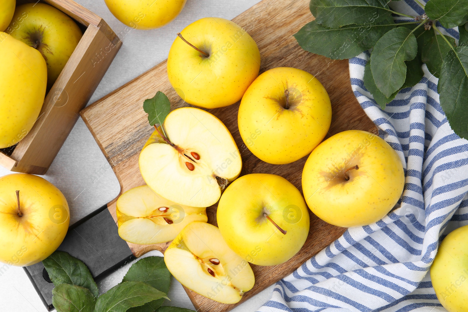 Photo of Ripe yellow apples and green leaves on light grey table, top view