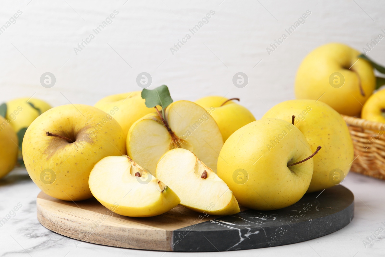 Photo of Ripe yellow apples and green leaves on white marble table, closeup