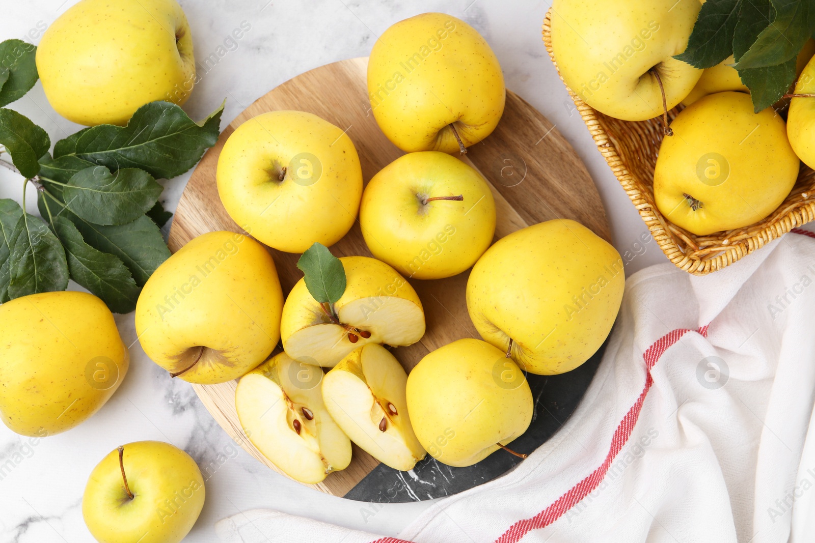 Photo of Ripe yellow apples and green leaves on white marble table, top view