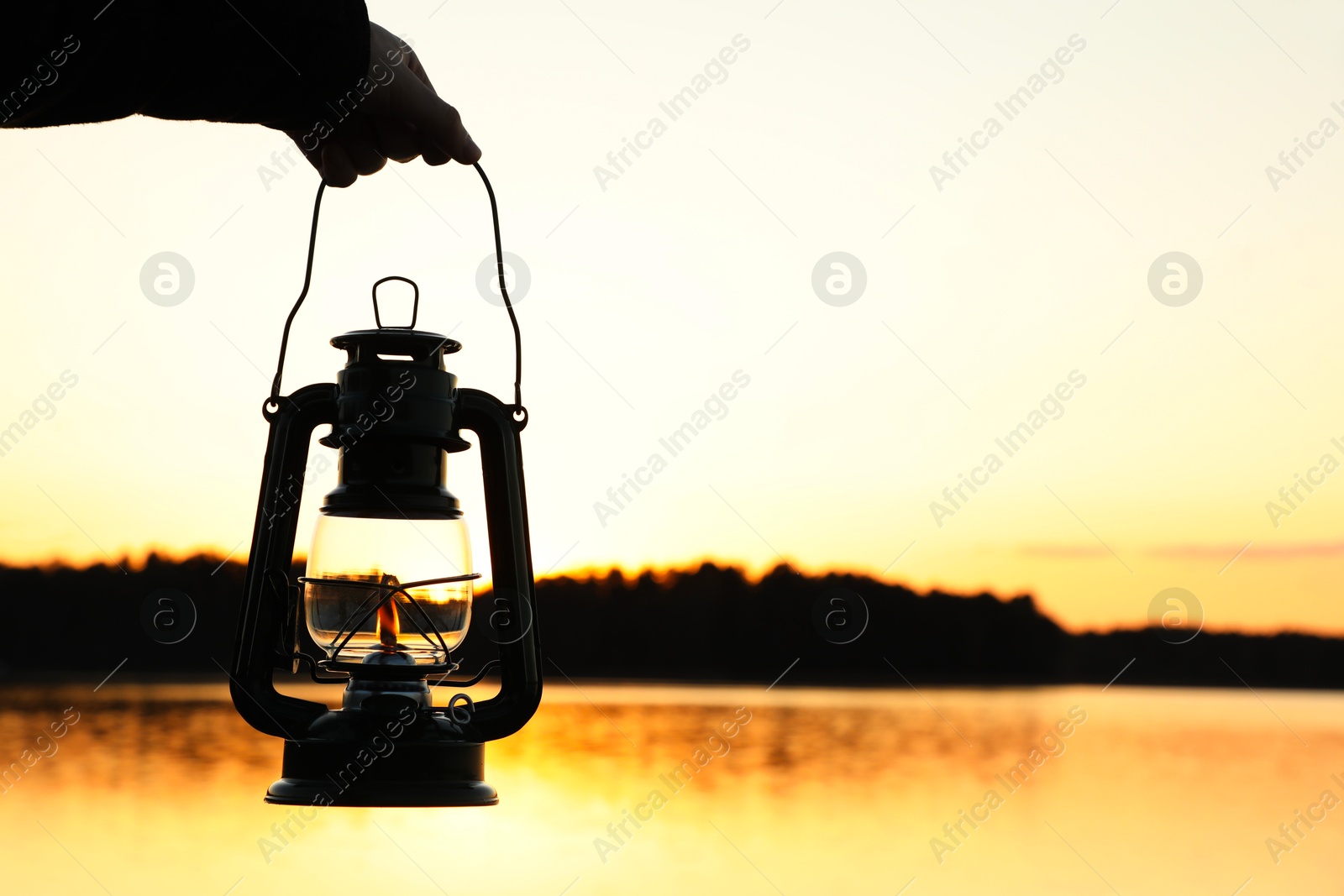 Photo of Man with vintage kerosene lamp near river in evening, closeup. Space for text