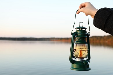 Photo of Man with vintage kerosene lamp near river in evening, closeup. Space for text