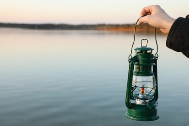 Photo of Man with vintage kerosene lamp near river in evening, closeup. Space for text