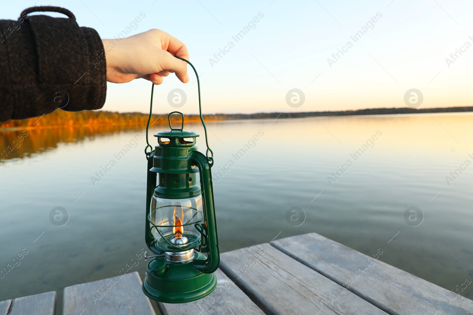 Photo of Man with vintage kerosene lamp near river in evening, closeup. Space for text