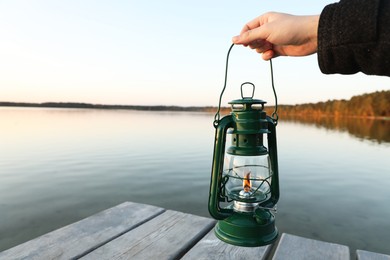 Photo of Man with vintage kerosene lamp near river in evening, closeup. Space for text