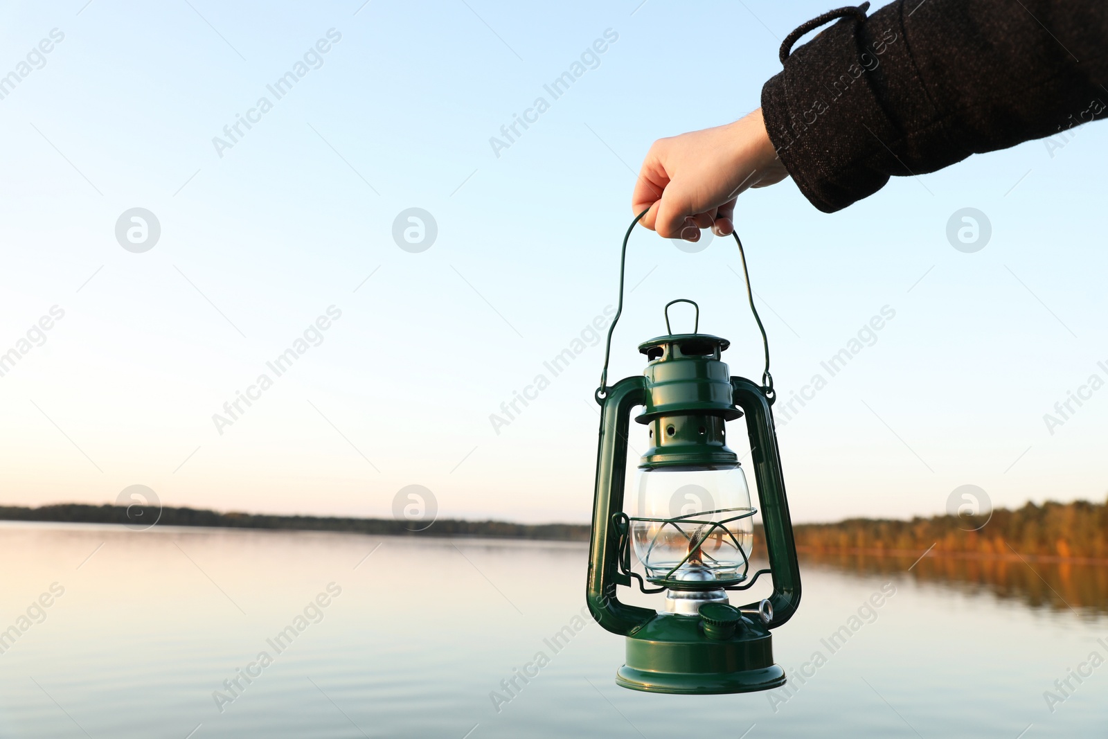 Photo of Man with vintage kerosene lamp near river in evening, closeup. Space for text