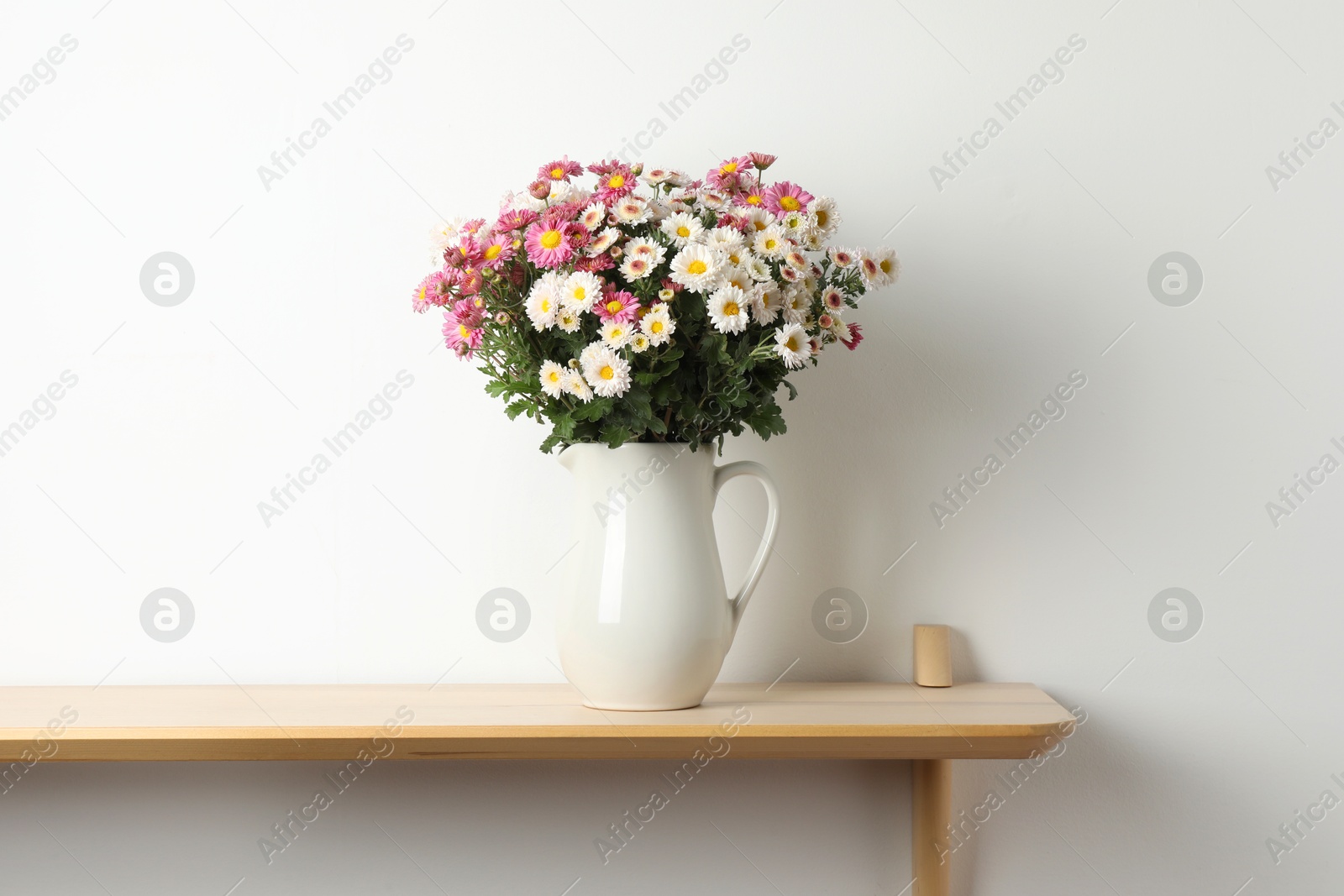 Photo of Vase with beautiful flowers on wooden shelf near white wall