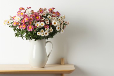 Photo of Vase with beautiful flowers on wooden shelf near white wall, space for text