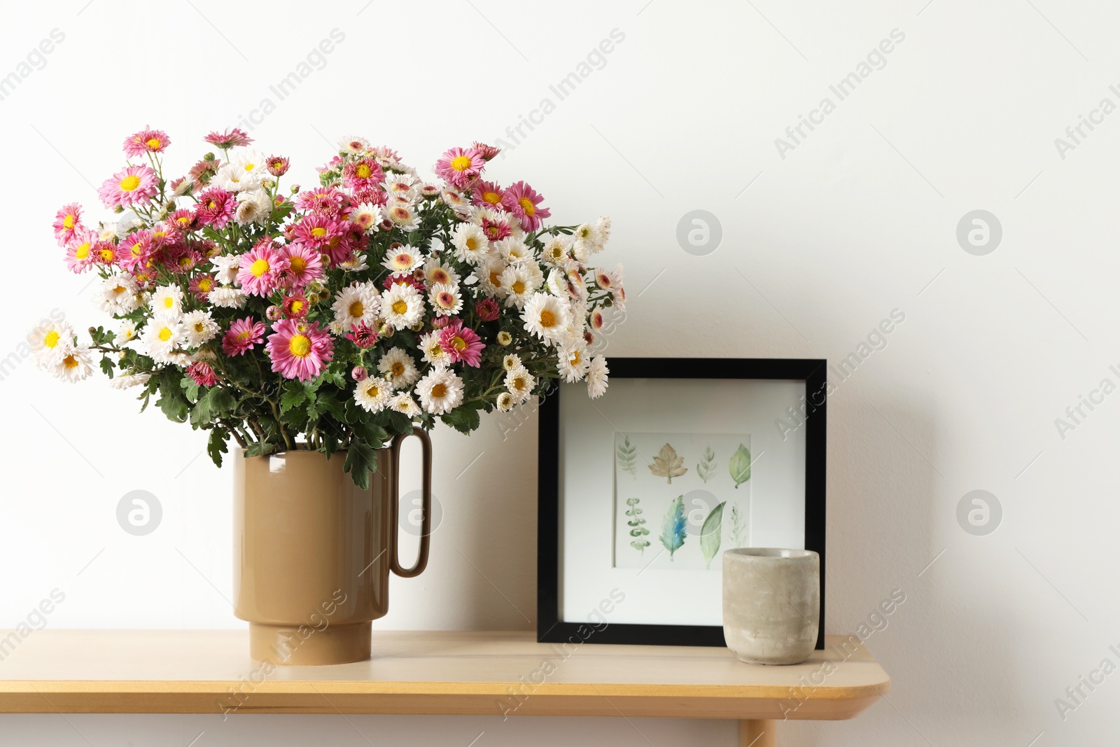 Photo of Vase with beautiful flowers and other decor on wooden shelf near white wall