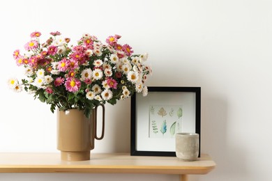 Photo of Vase with beautiful flowers and other decor on wooden shelf near white wall