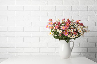 Photo of Vase with beautiful flowers on wooden table near white brick wall, space for text