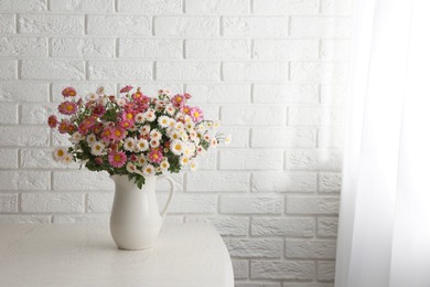 Photo of Vase with beautiful flowers on wooden table near white brick wall. Space for text