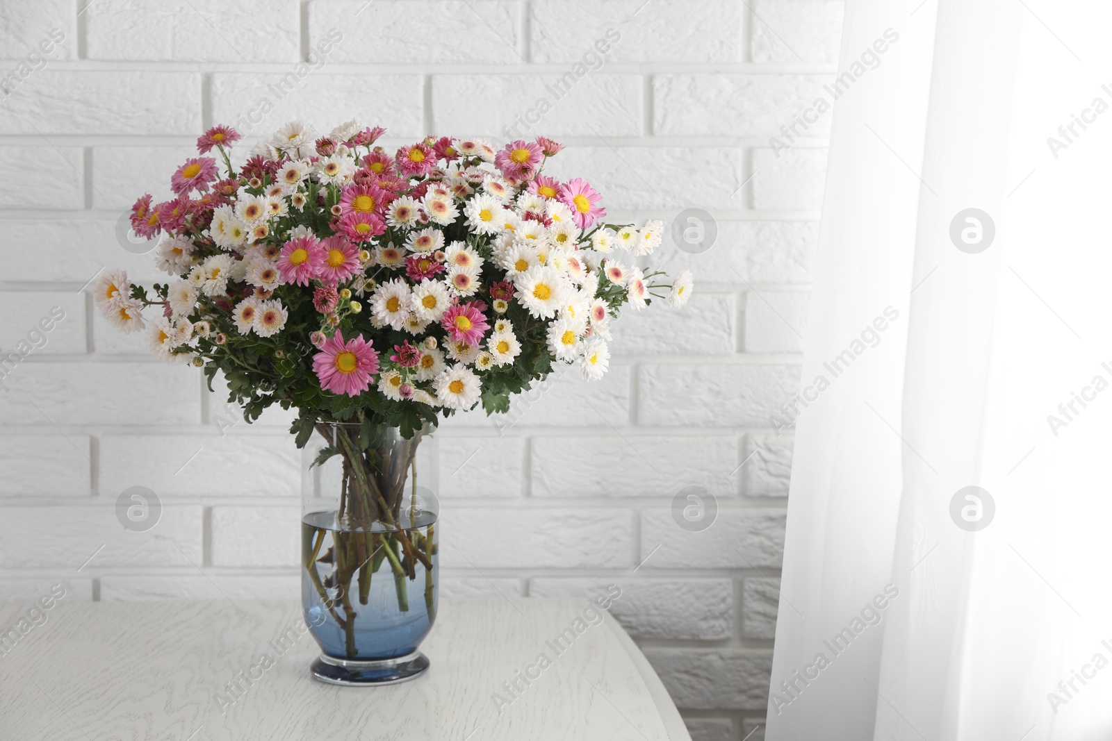 Photo of Vase with beautiful flowers on wooden table near white brick wall. Space for text