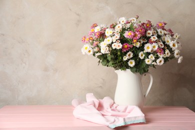 Photo of Vase with beautiful flowers and cloth on pink wooden table, space for text