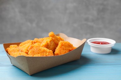 Photo of Delicious chicken nuggets in carton box and ketchup on light blue wooden table, closeup